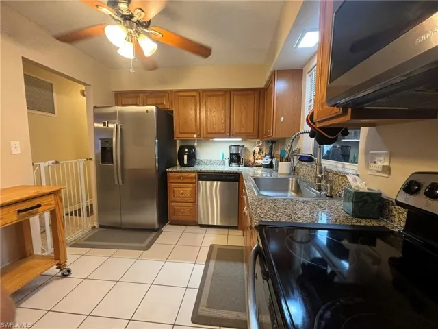 Kitchen featuring, tile flooring, stainless steel appliances, dark stone counters, and ceiling fan