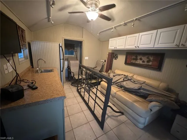 Kitchen with vaulted ceiling, sink, white cabinets, light tile patterned floors, and track lighting
