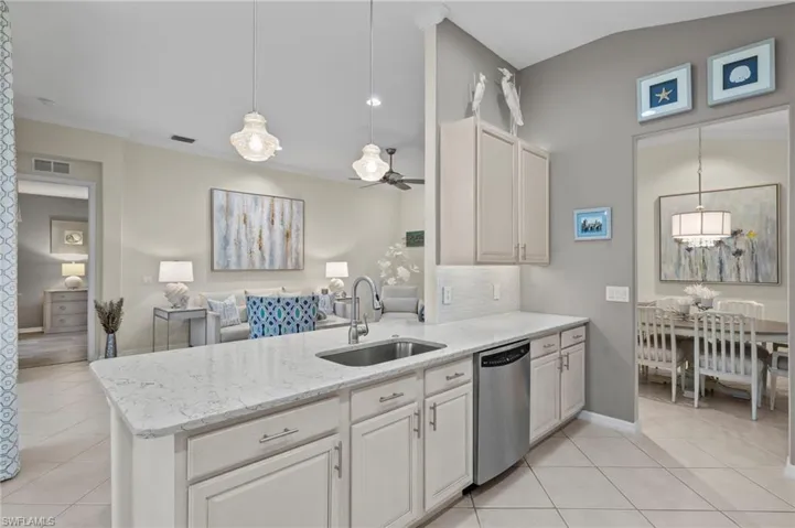 Kitchen with white cabinetry, sink, decorative light fixtures, lofted ceiling, and dishwasher