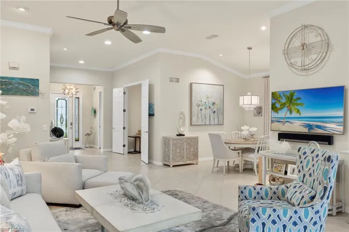 Tiled living room featuring ornamental molding, ceiling fan with notable chandelier, and lofted ceiling