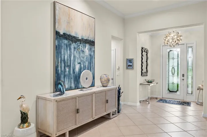 Foyer with light tile patterned flooring, an inviting chandelier, and crown molding