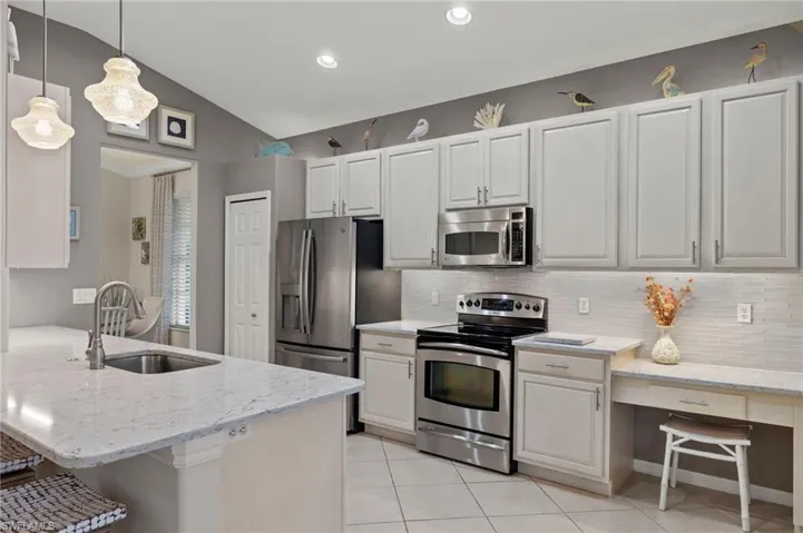 Kitchen with sink, kitchen peninsula, appliances with stainless steel finishes, hanging light fixtures, and lofted ceiling