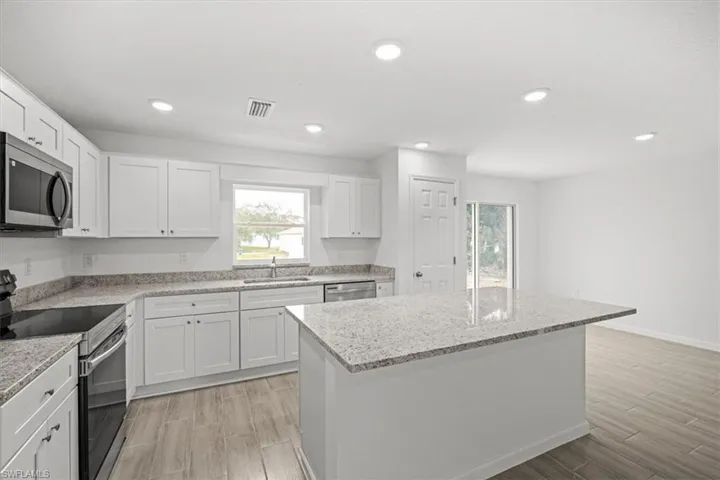 Kitchen with stainless steel appliances, wood tiled floors, a kitchen island, light stone countertops, and white cabinetry