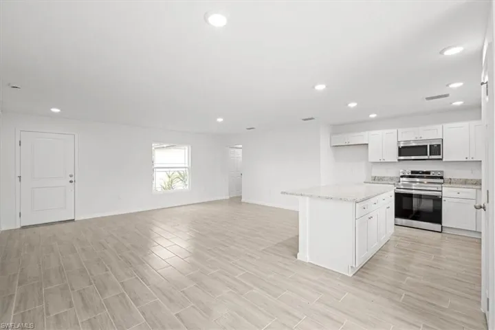 Kitchen featuring stainless steel appliances, a center island, open floor plan, white cabinetry, and light stone counters