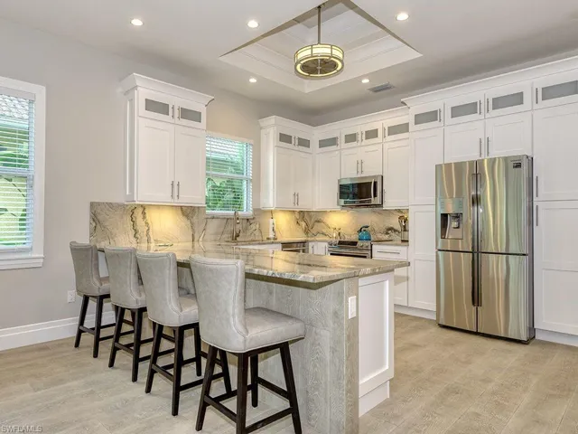 Kitchen featuring appliances with stainless steel finishes, light stone countertops, tasteful backsplash, white cabinets, and a kitchen bar