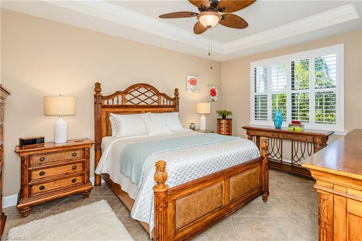 Bedroom with ornamental molding, a raised ceiling, a ceiling fan, and baseboards