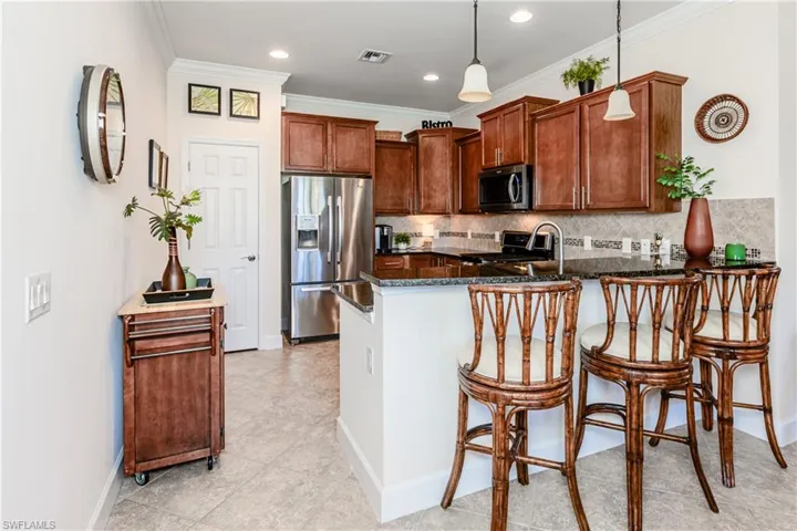 Kitchen featuring tasteful backsplash, dark stone counters, appliances with stainless steel finishes, ornamental molding, and a peninsula