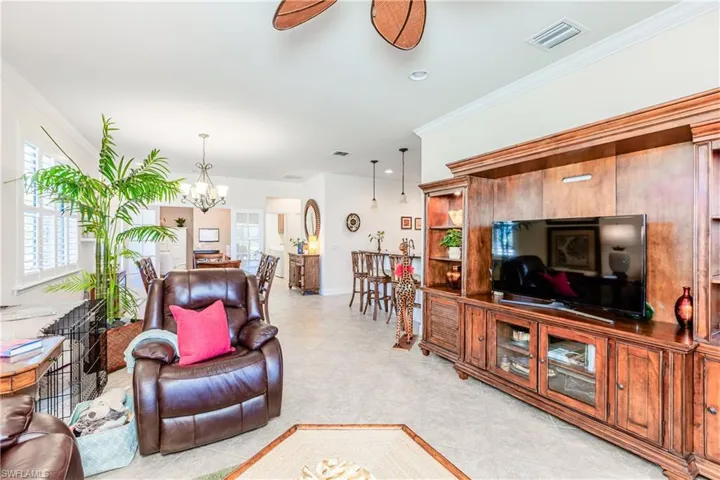 Living room featuring ceiling fan with notable chandelier, ornamental molding, visible vents, and baseboards