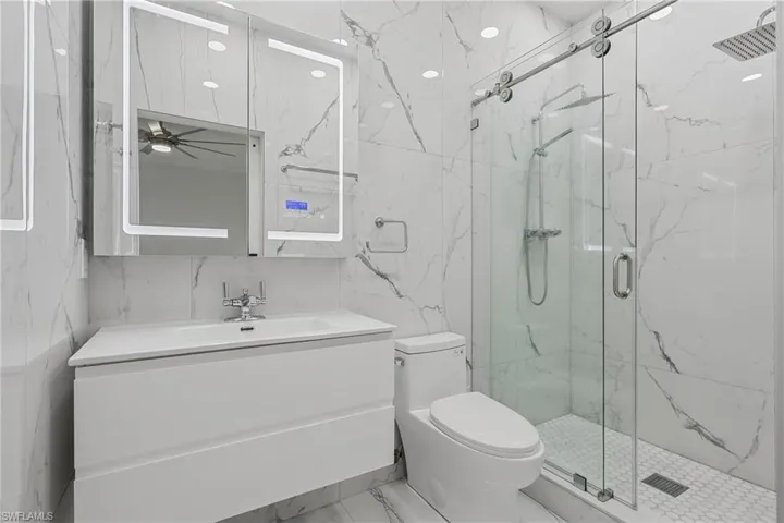 White floating vanity with integrated sink, illuminated medicine cabinet, walk-in shower with sliding glass door, and wall-mounted rain shower head