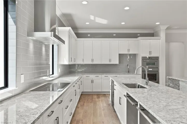 Kitchen featuring wall chimney exhaust hood, white cabinets, appliances with stainless steel finishes, light stone counters, and tasteful backsplash
