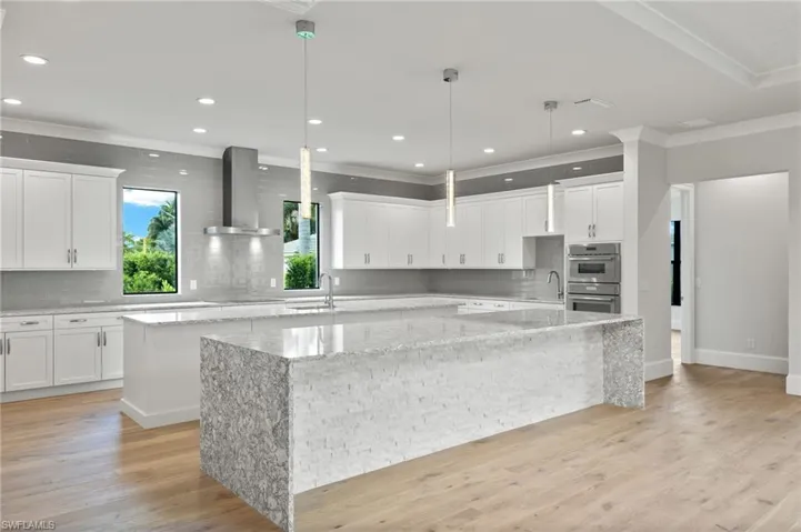 Kitchen featuring wall chimney range hood, light stone counters, a large island, light hardwood / wood-style floors, and crown molding