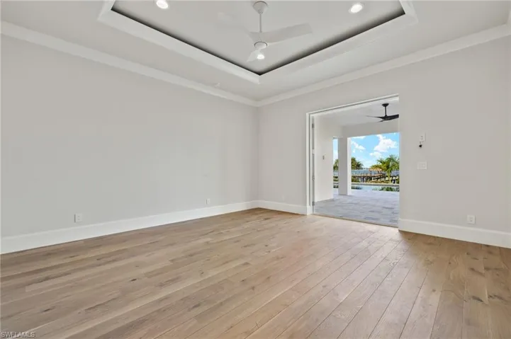 Spare room with ceiling fan, crown molding, a tray ceiling, and light wood-type flooring
