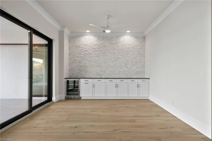 Bar with crown molding, light wood-type flooring, white cabinetry, ceiling fan, and wine cooler