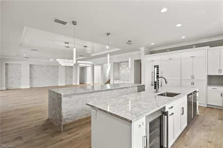 Kitchen featuring a large island, beverage cooler, white cabinetry, sink, and decorative light fixtures
