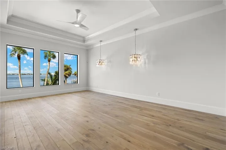 Empty room with ceiling fan with notable chandelier, a tray ceiling, a water view, and light wood-type flooring