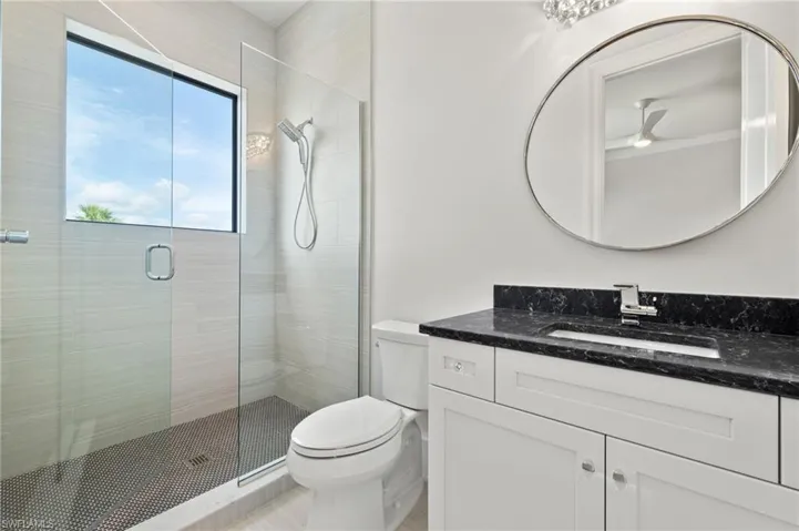 Bathroom featuring a shower with door, toilet, ceiling fan, and vanity