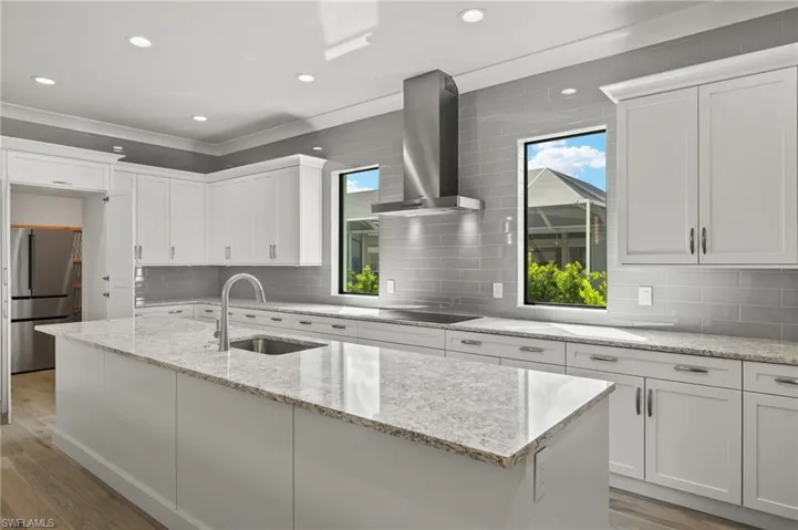Kitchen with light hardwood / wood-style floors, wall chimney exhaust hood, sink, and stainless steel refrigerator