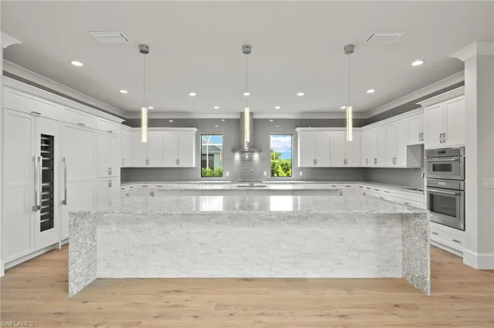 Kitchen with a spacious island, light stone counters, white cabinetry, and stainless steel double oven