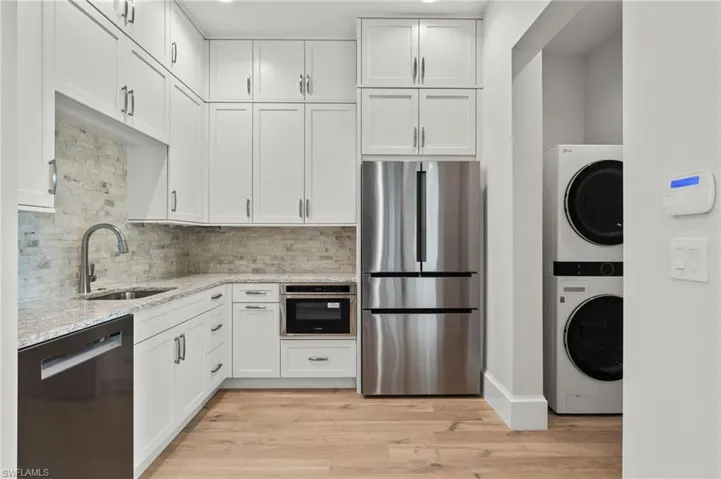 Kitchen featuring appliances with stainless steel finishes, white cabinets, stacked washer and dryer, and sink