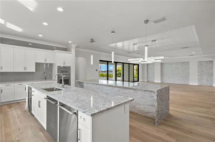 Kitchen with light hardwood / wood-style flooring, white cabinetry, pendant lighting, and a large island with sink