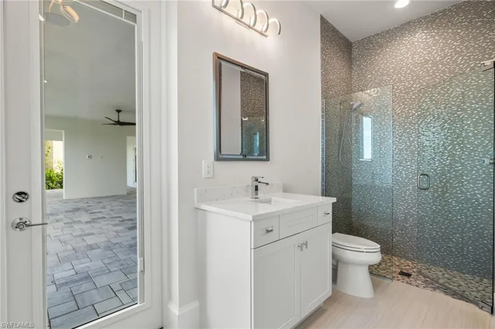 Bathroom with ceiling fan, a shower with door, toilet, vanity, and tile patterned floors