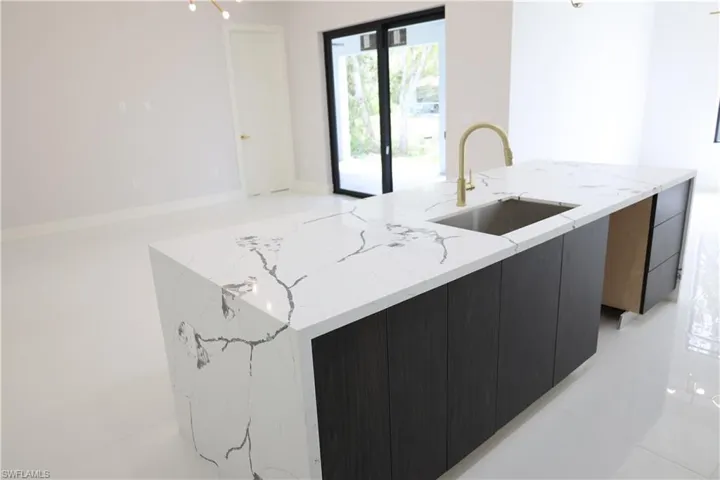 Kitchen featuring a spacious island, a sink, light stone counters, modern cabinets, and dark cabinets