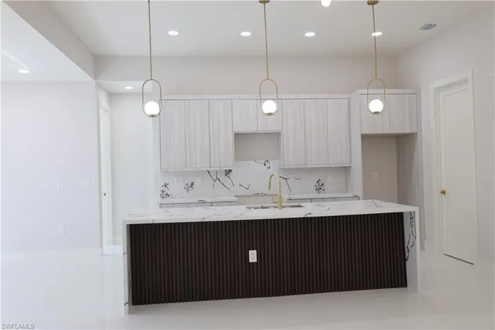 Kitchen featuring tasteful backsplash, light stone countertops, a center island with sink, modern cabinets, and a sink