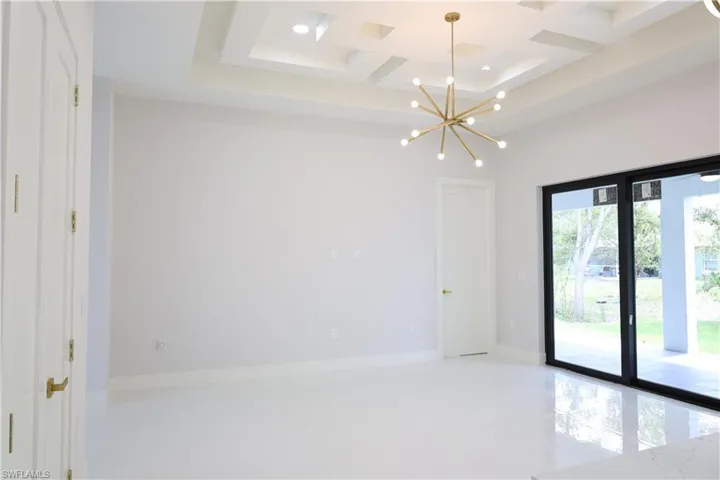 Empty room featuring beam ceiling, coffered ceiling, baseboards, and an inviting chandelier