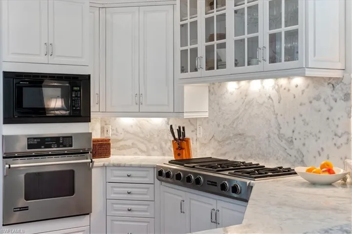 Kitchen featuring stainless steel appliances, white cabinetry, glass insert cabinets, and backsplash