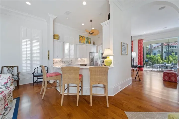 Kitchen featuring wood finished floors, light countertops, stainless steel refrigerator with ice dispenser, decorative backsplash, and crown molding