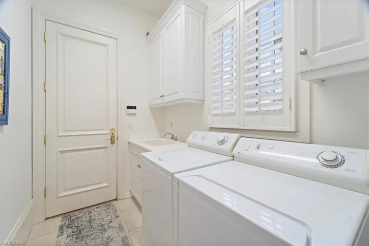 Laundry room with a sink, light tile patterned floors, washing machine and clothes dryer, and cabinet space