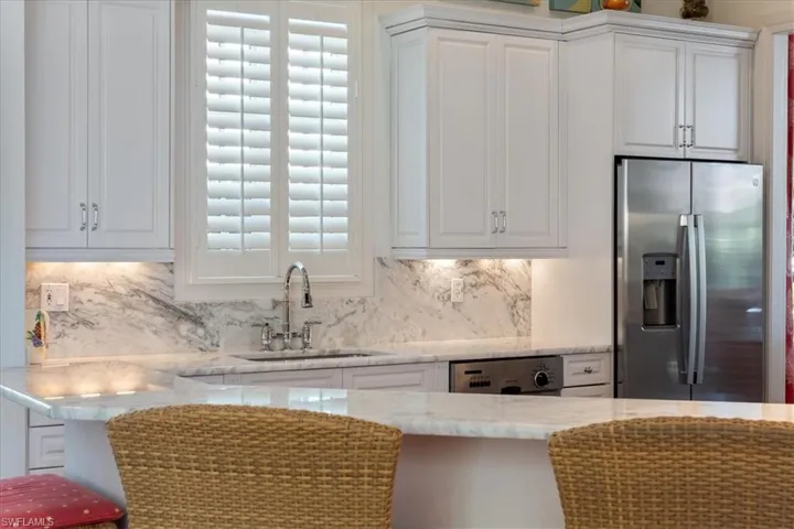 Kitchen with a sink, white cabinets, stainless steel refrigerator with ice dispenser, backsplash, and dishwasher