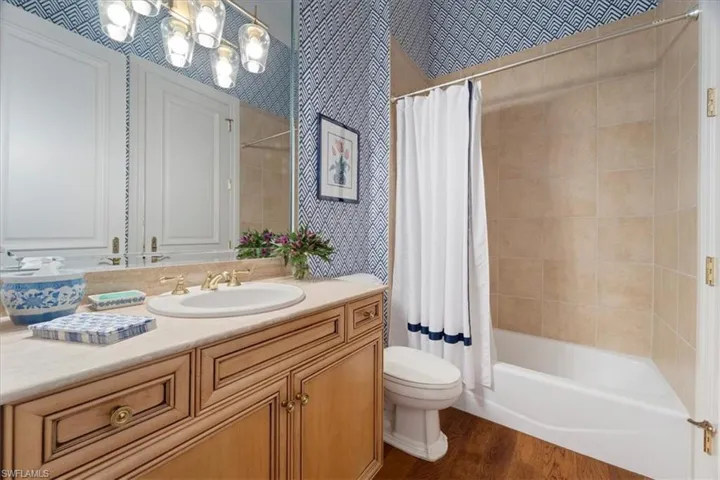 Bathroom with toilet, wood finished floors, shower / bath combination with curtain, vanity, and a notable chandelier