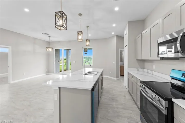 Kitchen featuring stainless steel appliances, recessed lighting, hanging light fixtures, light stone countertops, and an island with sink
