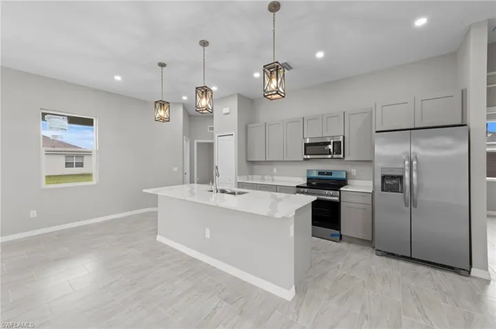 Kitchen featuring appliances with stainless steel finishes, gray cabinets, light stone counters, a kitchen island with sink, and hanging light fixtures
