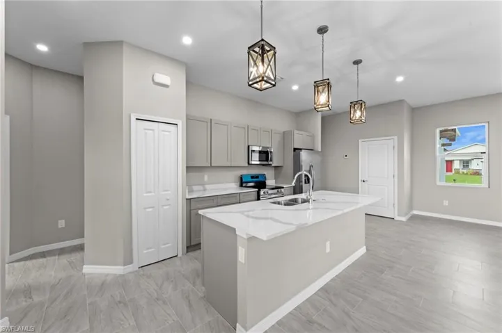 Kitchen featuring gray cabinetry, an island with sink, pendant lighting, stainless steel appliances, and light stone counters