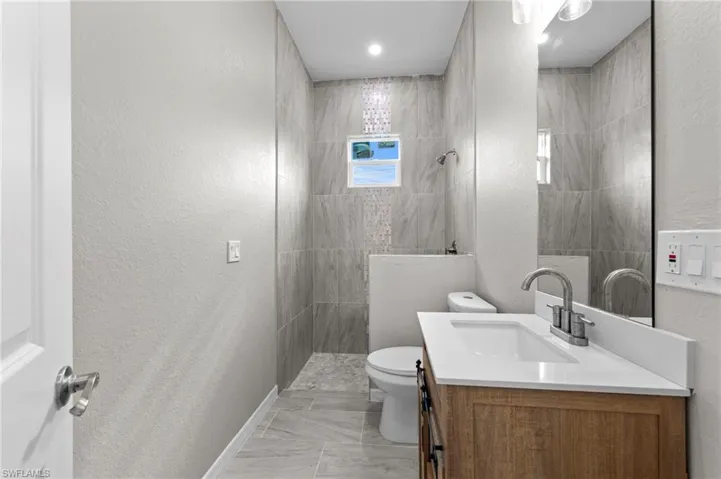 Full bathroom featuring a textured wall, walk in shower, vanity, and light marble finish floors