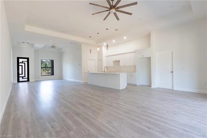 Unfurnished living room featuring ceiling fan, light wood finished floors, recessed lighting, and a tray ceiling