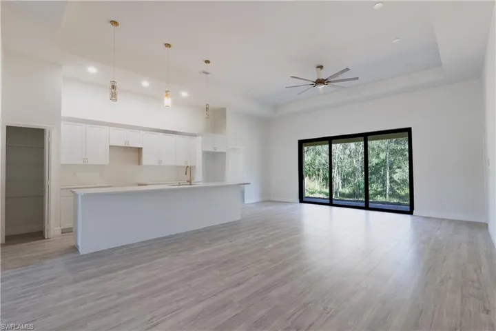 Unfurnished living room with ceiling fan, light wood-type flooring, and a raised ceiling
