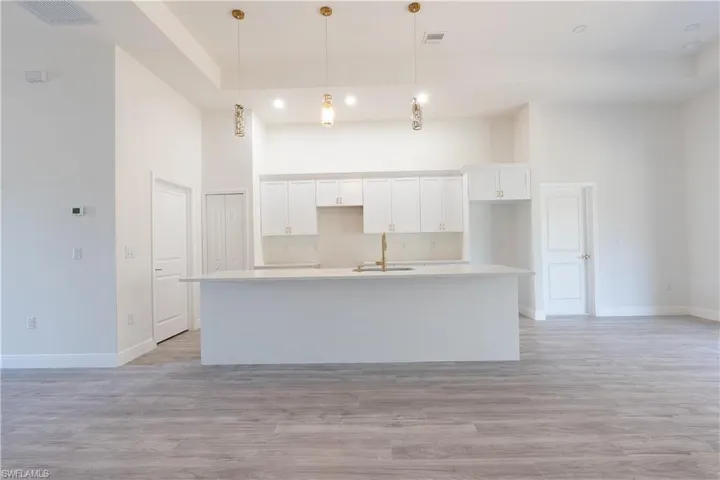 Kitchen with white cabinets, a high ceiling, light wood finished floors, decorative light fixtures, and an island with sink