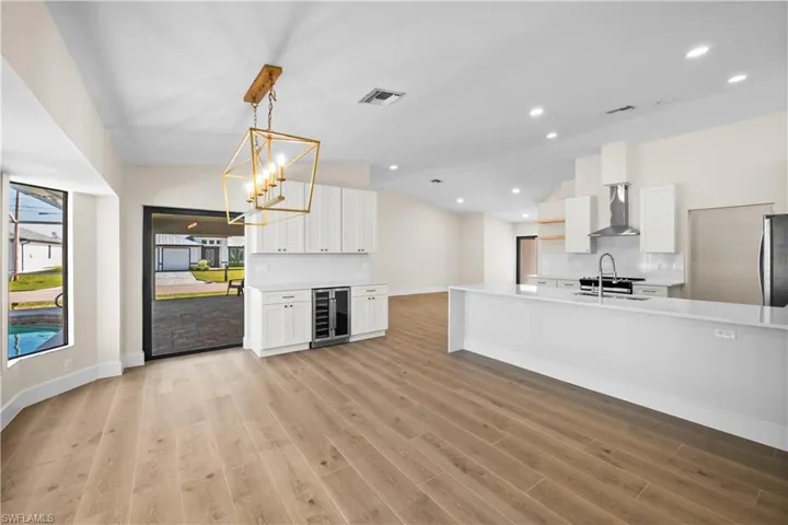 Kitchen with a wealth of natural light, white cabinetry, wall chimney exhaust hood, and hanging light fixtures