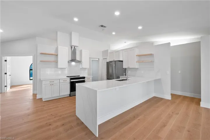 Kitchen with white cabinetry, stainless steel appliances, wall chimney range hood, kitchen peninsula, and light hardwood / wood-style floors