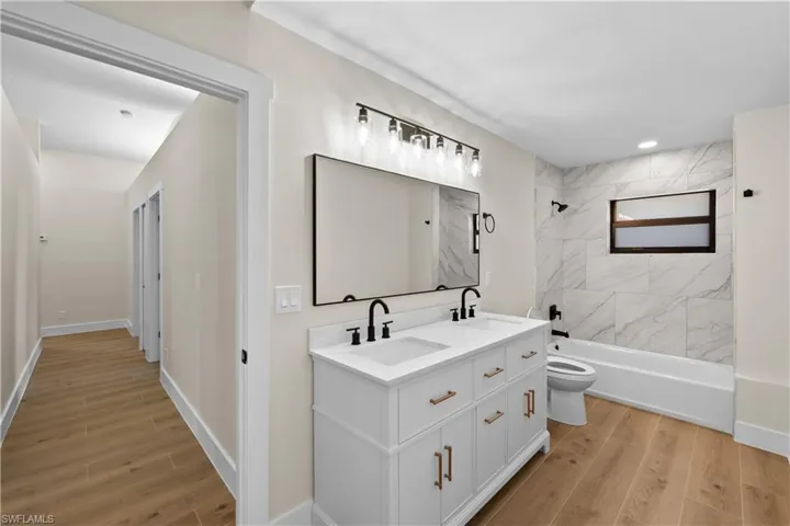 Full bathroom with vanity, wood-type flooring, tiled shower / bath combo, and toilet