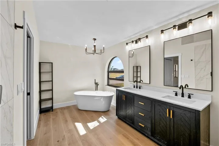 Bathroom featuring hardwood / wood-style flooring, a notable chandelier, a tub to relax in, and vanity