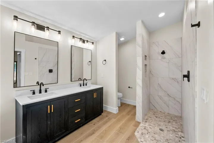 Bathroom featuring tiled shower, vanity, hardwood / wood-style flooring, and toilet