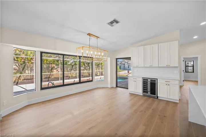 Kitchen featuring decorative light fixtures, white cabinetry, beverage cooler, and plenty of natural light