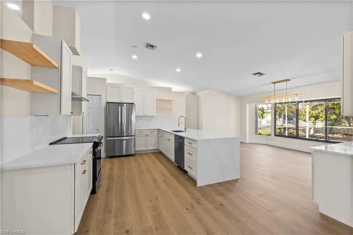 Kitchen with kitchen peninsula, stainless steel appliances, vaulted ceiling, decorative light fixtures, and white cabinets