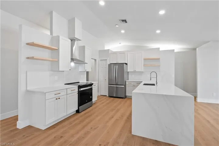 Kitchen featuring light wood-type flooring, wall chimney exhaust hood, stainless steel appliances, sink, and white cabinetry
