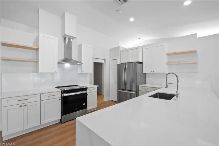 Kitchen featuring white cabinets, wall chimney exhaust hood, sink, and appliances with stainless steel finishes