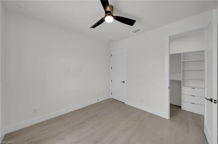 Unfurnished bedroom with light wood finished floors, a walk in closet, baseboards, a ceiling fan, and a closet